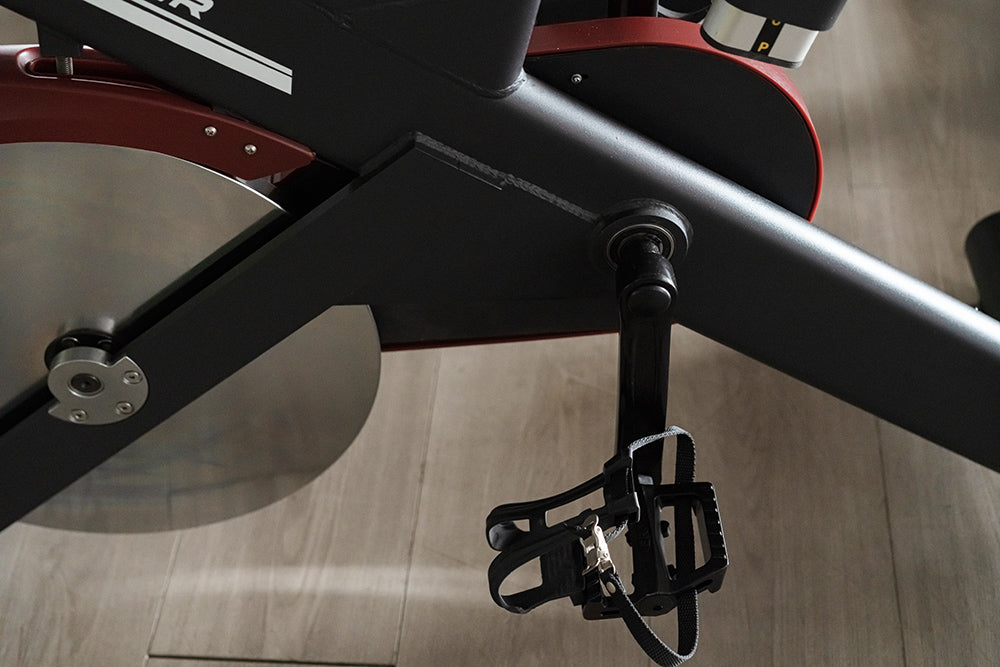 Close-up of a spine bike's pedal and frame on a wooden floor.