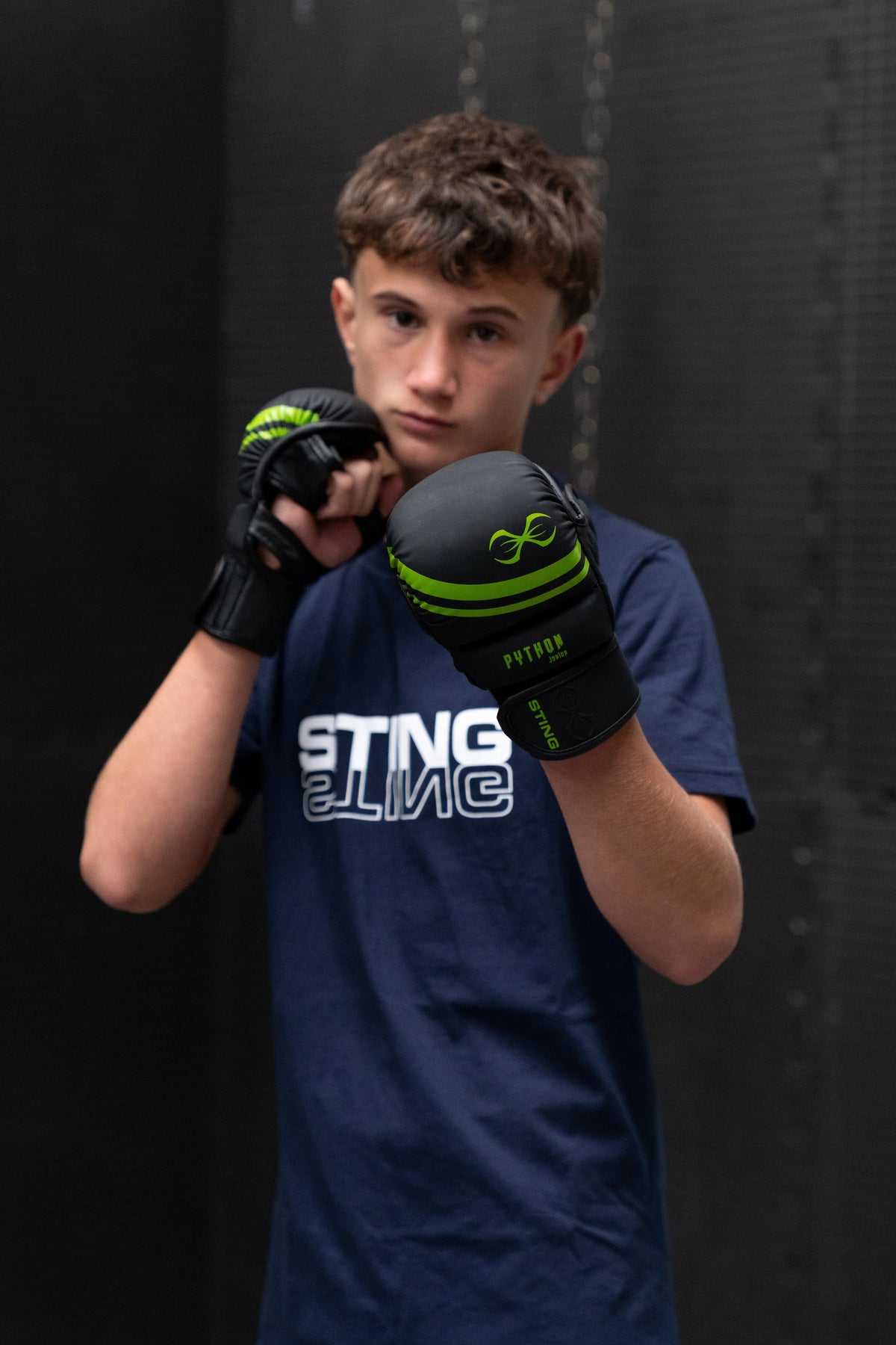 Person wearing junior mma gloves 4oz sparring gloves black green gloves and a blue shirt with text