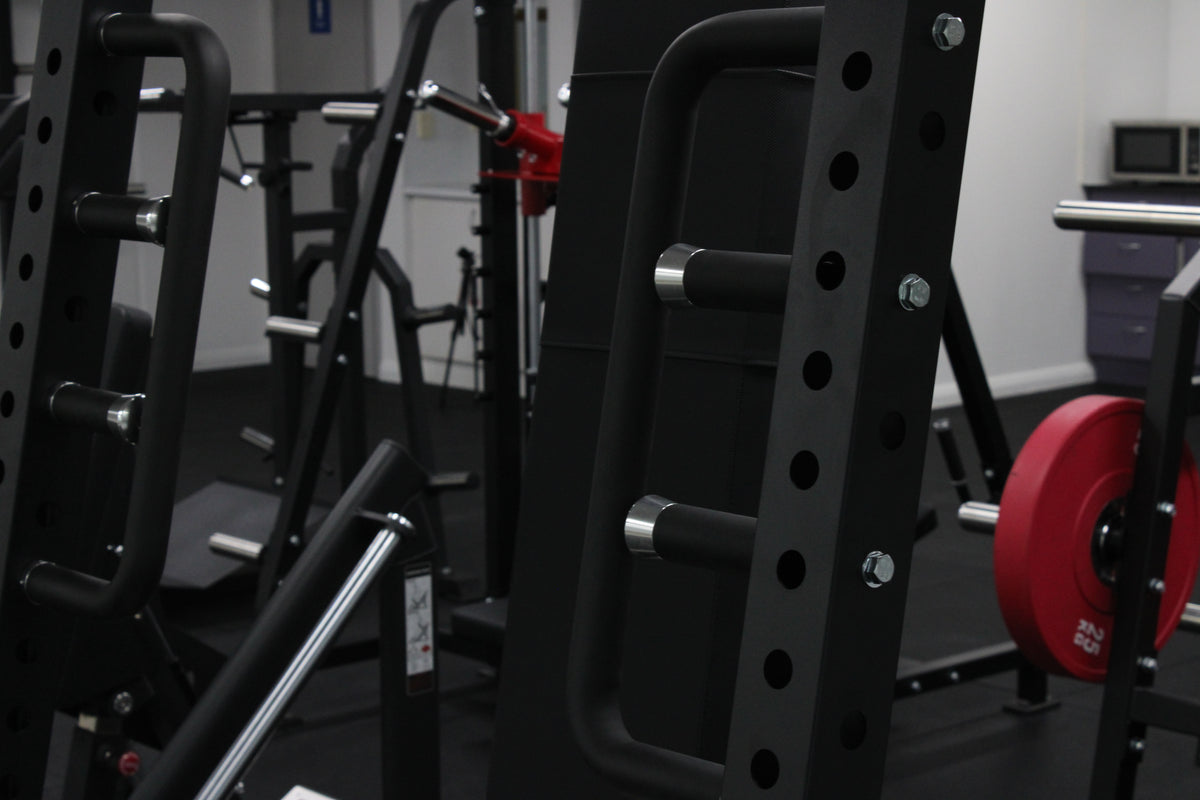 Standing chest press Coffin Press machine on the gym floor showing multiple handle heights and grip positions.