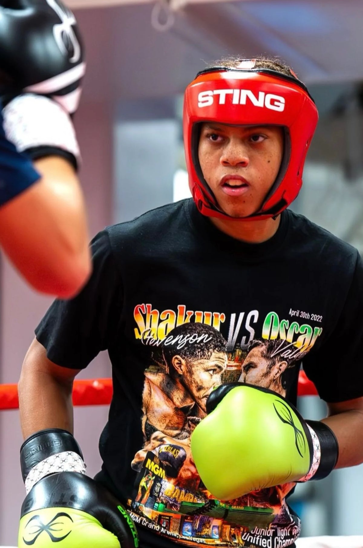 Boxer in a red sting helmet and black shirt with boxing gloves in a boxing ring.