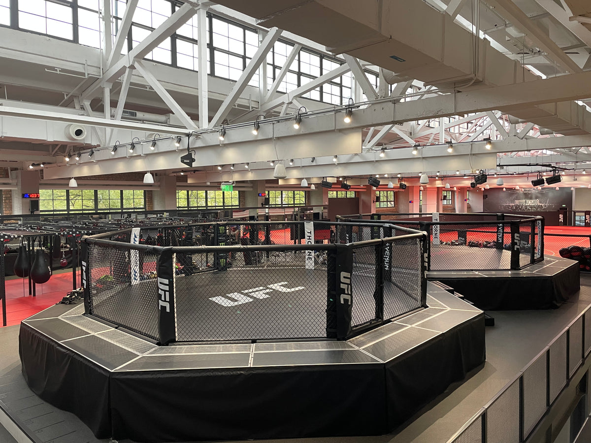 UFC octagon in a large indoor sports facility with multiple training rings.