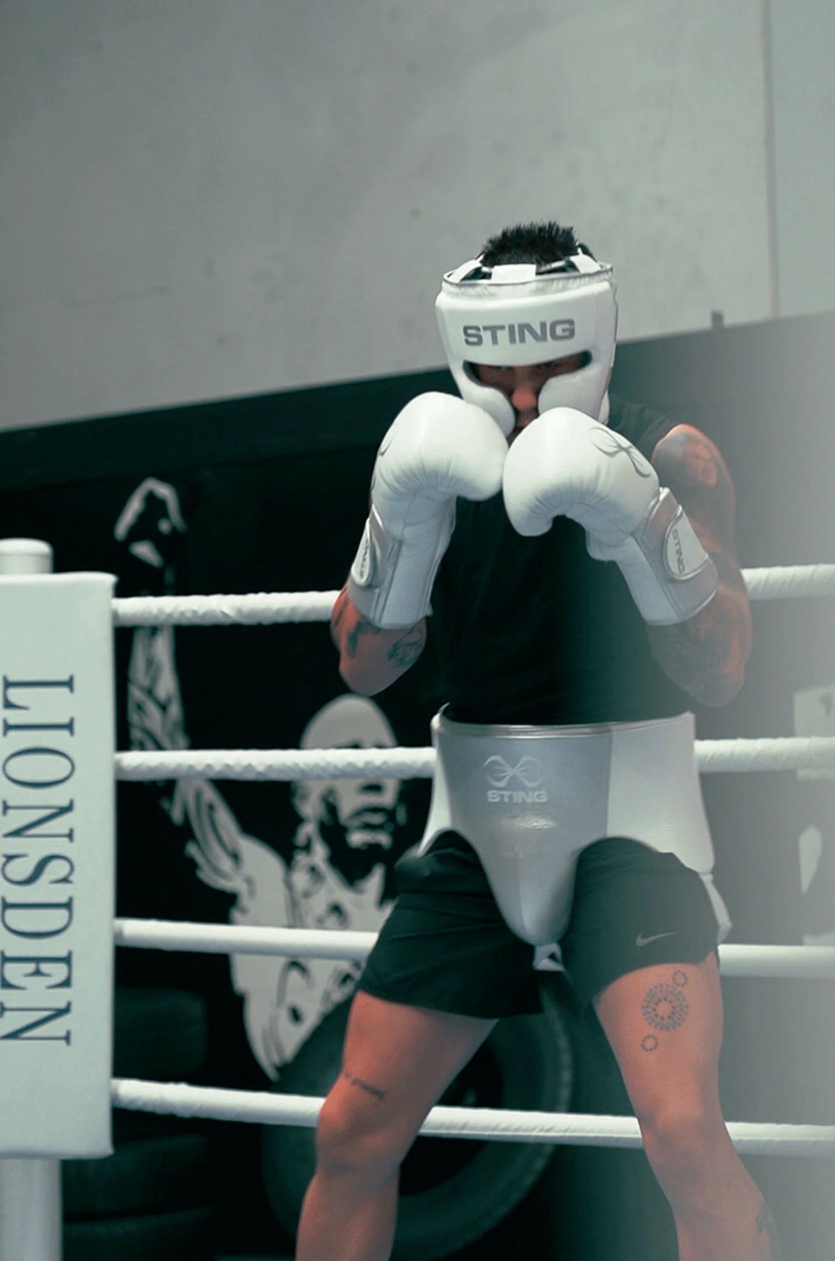 Boxer in a white Sting helmet and gloves sitting on a boxing ring.